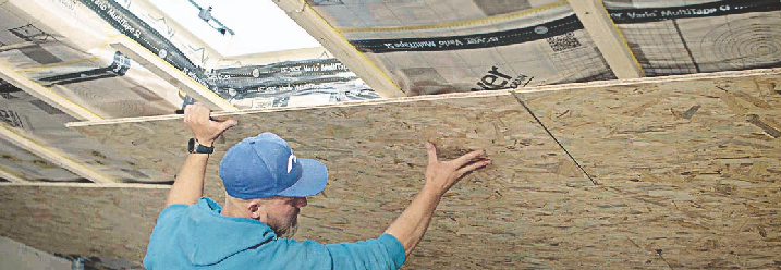 Ein Handwerker hält OSB-Platten an die Dachschräge, um die Dachschräge damit zu verkleiden.